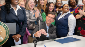 Governor Bob Ferguson points to an executive order as a group of women cheer and applaud.