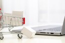 Tiny shopping cart with tiny packages on a table next to a laptop - Online Shopping Concept