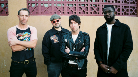 Four men stand in front of a beige stone wall