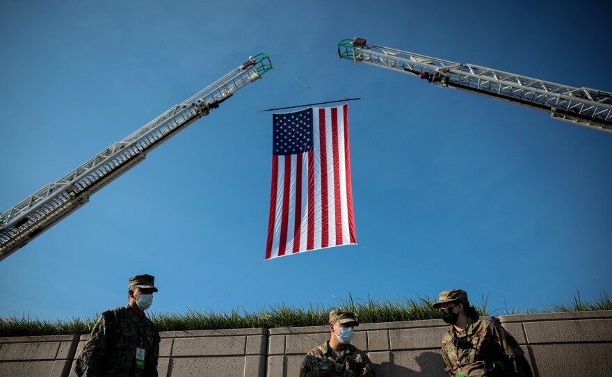 Soldiers wait below an American flag prior to the start of the Pentagon 9/11 observance ceremony at the National 9/11 Pentagon Memorial on Saturday in Arlington, Va.