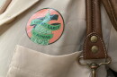 A close-up of an "I voted early in Athens" sticker on someone's beige blouse, next to the brown leather straps of their handbag. 