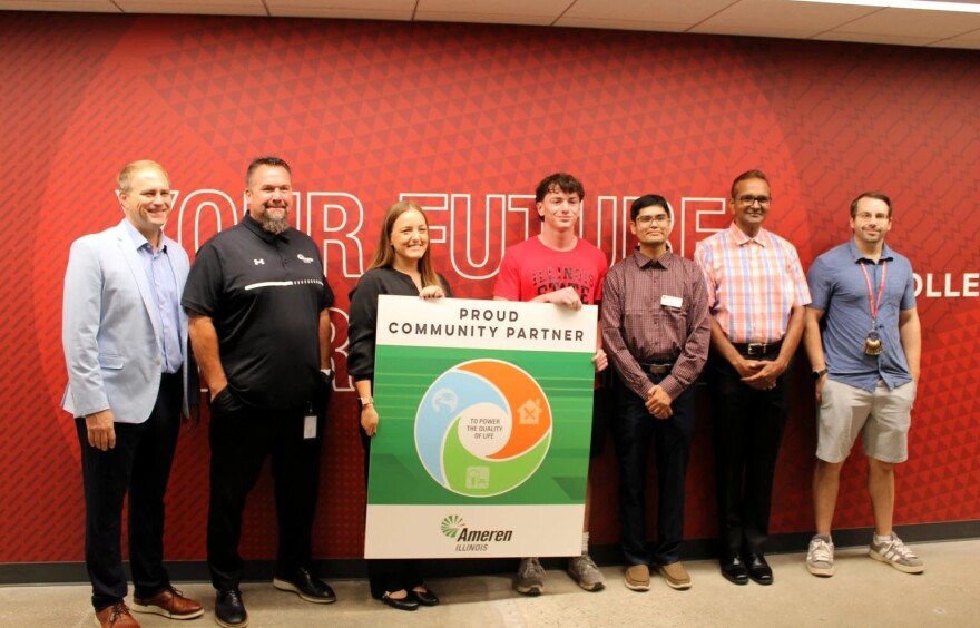 A group of people stand in front of a red wall holding a Ameren partner sign.