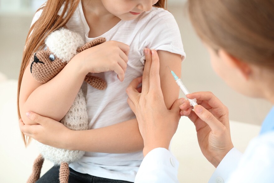 A doctor vaccinates a little girl in her arm as the child holds a stuffed animal