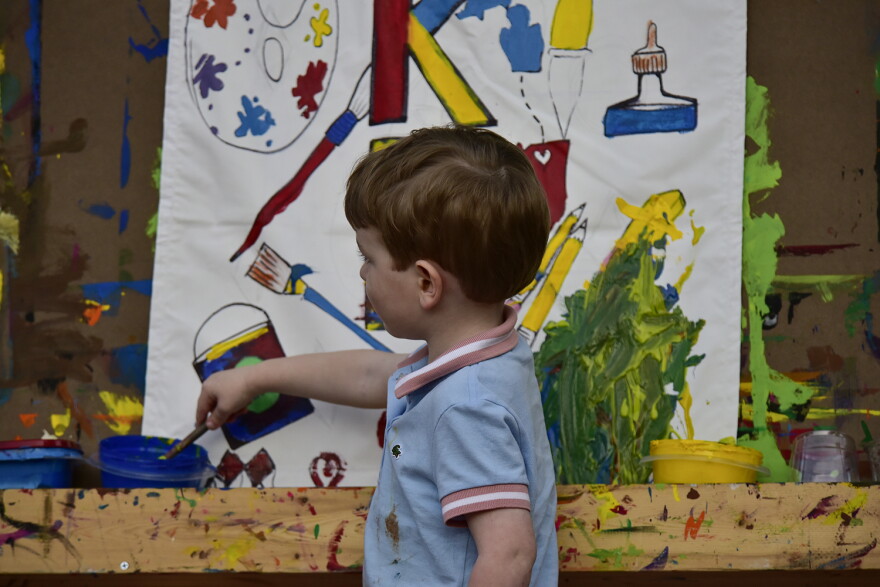 A child plays with paint on a canvas.