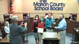 Supervisor of Elections Wesley Wilcox, second from right, presents a trophy to North Marion High School U.S. government teacher Michael Hill Tuesday night. Image: MCPS via video