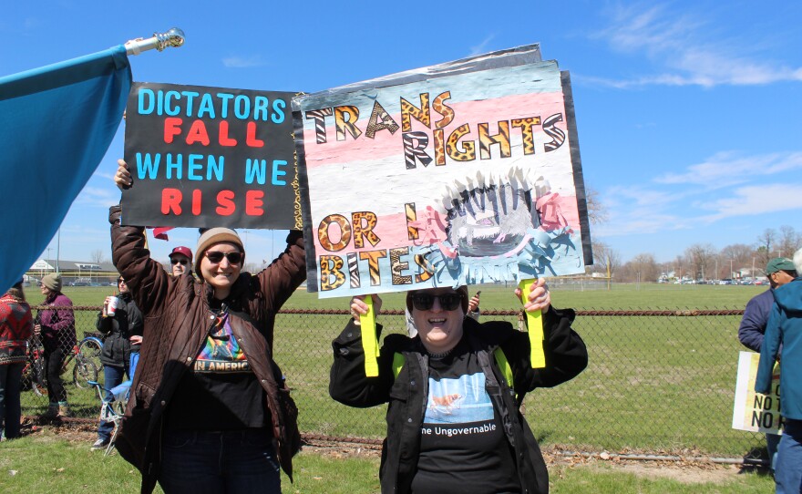 David Shuford (right) and friend from Peoria hold signs at the "No Kings" Protest reading "Dictators fall when we rise." and "Trans Rights or I Bite."