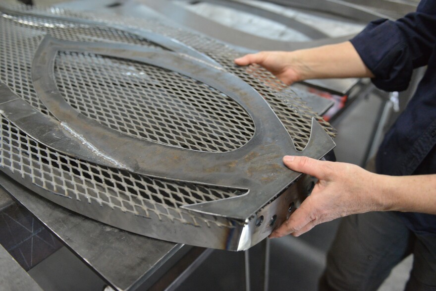 A pair of hands hold a gray steel frame and sheet metal that are roughly shaped like a flower petal.