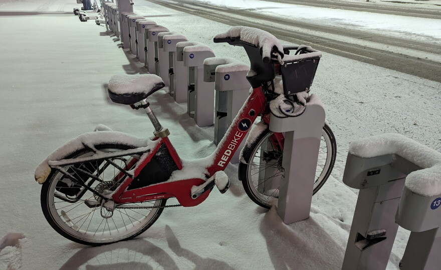 A snow covered Red Bike sits alone in a docking station along Mehring Way, in the predawn hours of January 19, 2024.