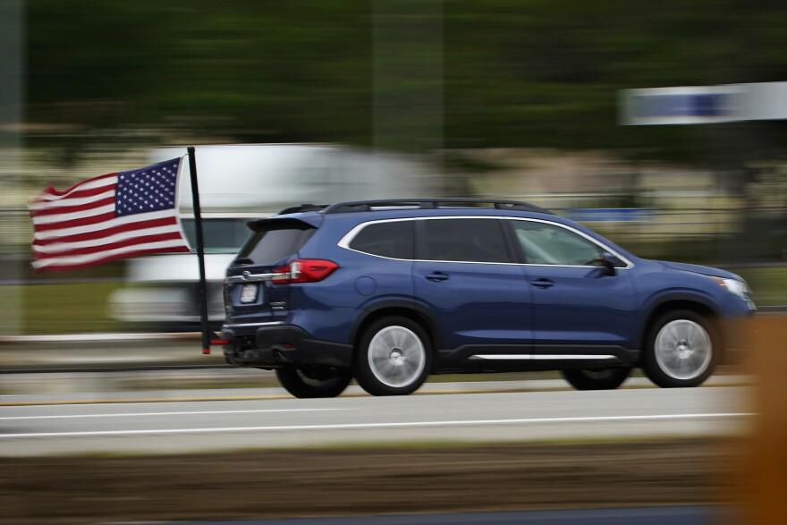 A motorist from Massachusetts flies an American flag ahead of the Memorial Day holiday while traveling on the Maine Turnpike, Friday, May 28, 2021, in Kennebunk, Maine. The state expects a large increase in the number of out-of-state visitors over last year when the COVID-19 pandemic forced a lot of businesses to close.