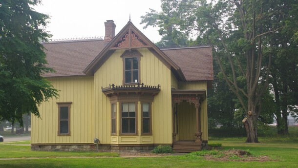 A yellow two story wood house stands on a green grass lawn. A thick blanket of fog looms around it. 