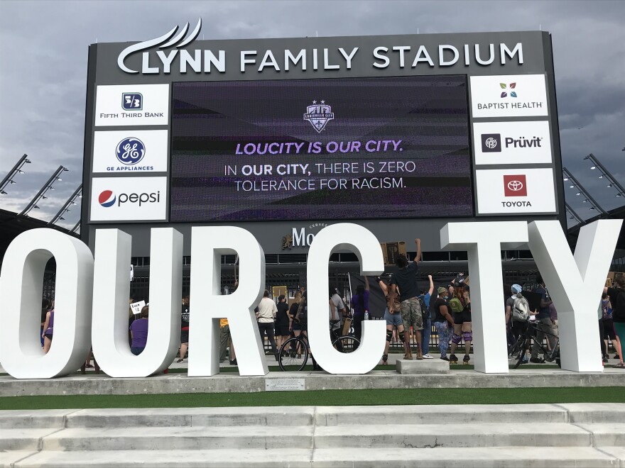A protester stands with his fist in the air completing the “I” in our city outside the Louisville City FC game.