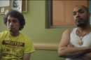 Alex sits in a yellow tee shirt with a red design and Dylan sits in a white cut off shirt and flashy gold chain.
