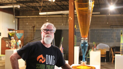 A man in a black t-shirt poses with a giant art sculpture made of glass