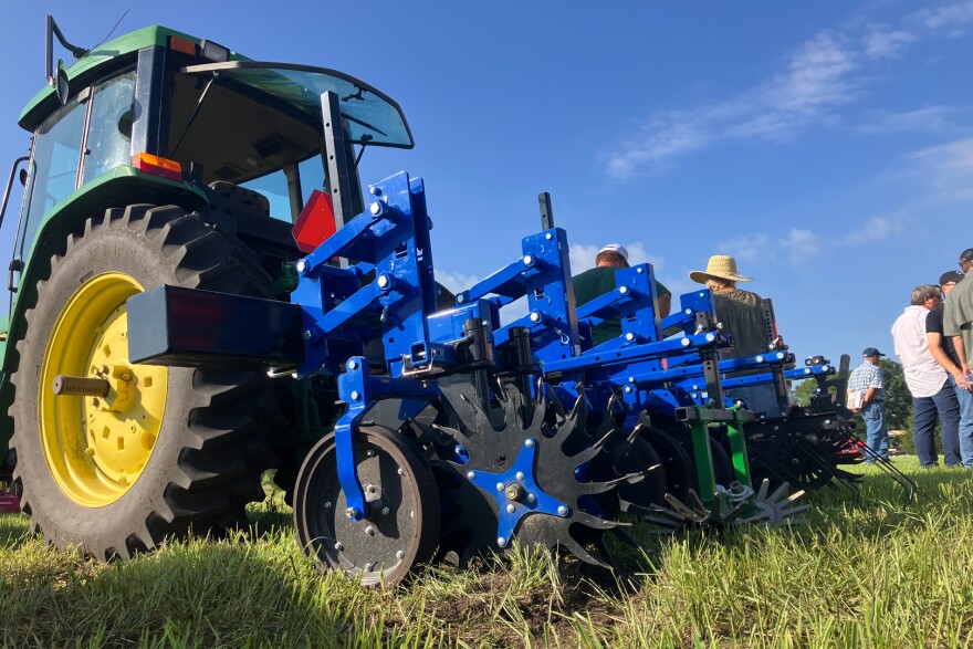 A green John Deere tractor has a blue metal attachment with finger weeders.