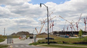A construction vehicle enters Intel's One Ohio manufacturing site through a gate. Mounds of dirt rise on the horizon, and dozens of tall construction cranes tower over a partially built building. 