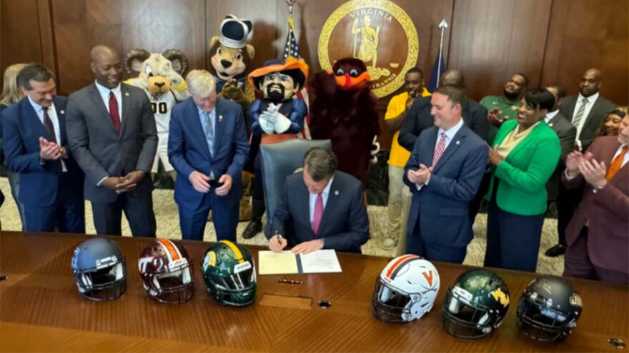 Governor Glenn Youngkin signs a bill allowing colleges to pay student athletes for their name, image and likeness. He's flanked to the left by Del. Terry Kilgore, Sen. Aaron Rouse and Del. Terry Austin. (Photo by Brad Kutner, Radio IQ)