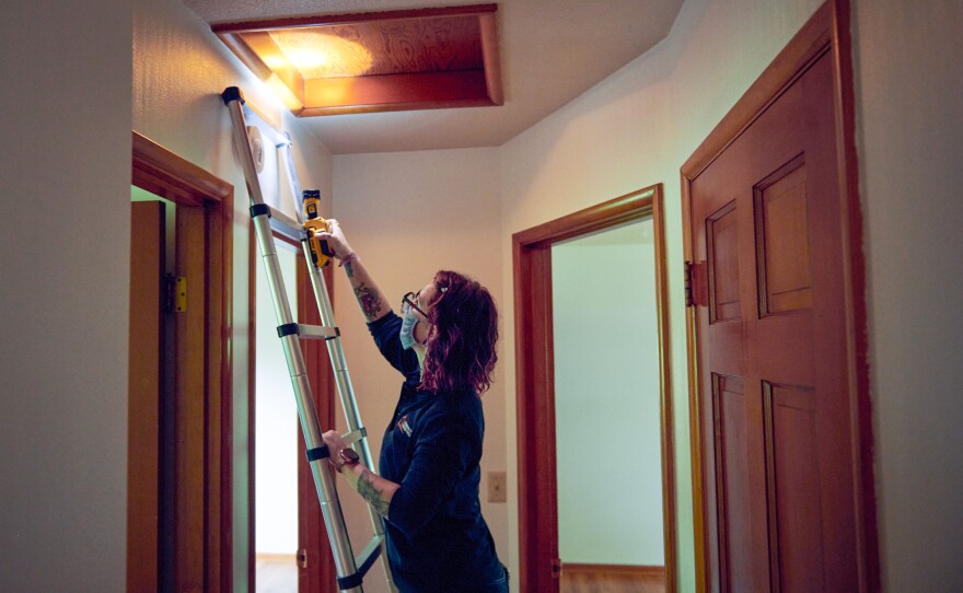 Home assessor Jackie Zusi-Russell conducts a home energy audit in a home in Portland, which includes going into the attic to check the insulation depth and type.