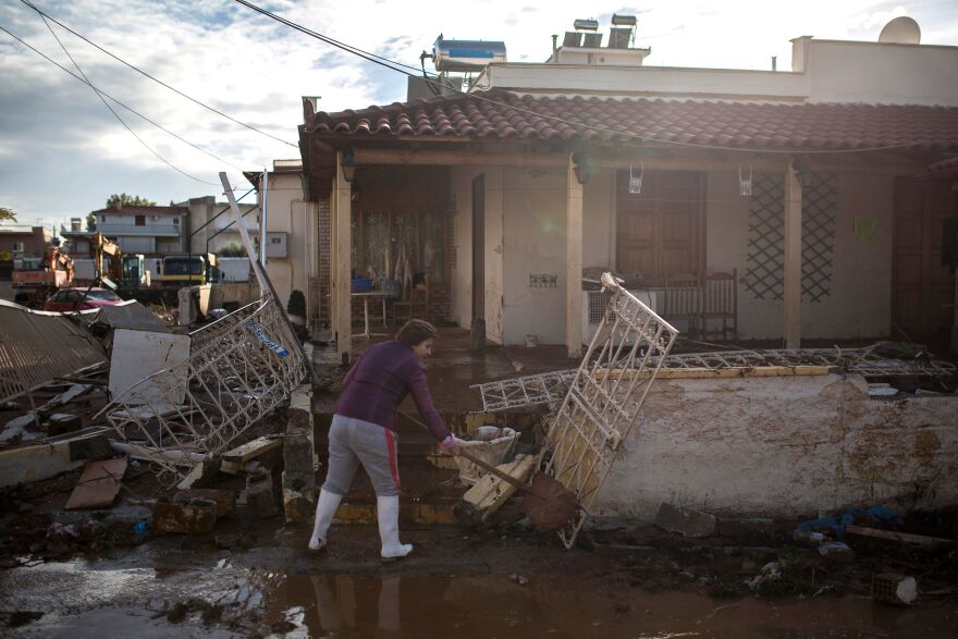 Flash floods killed at least 20 people in Greece, in a storm some were calling a "medicane." A woman cleans mud in front of a house in the town of Mandra, northwest of Athens, on Friday.