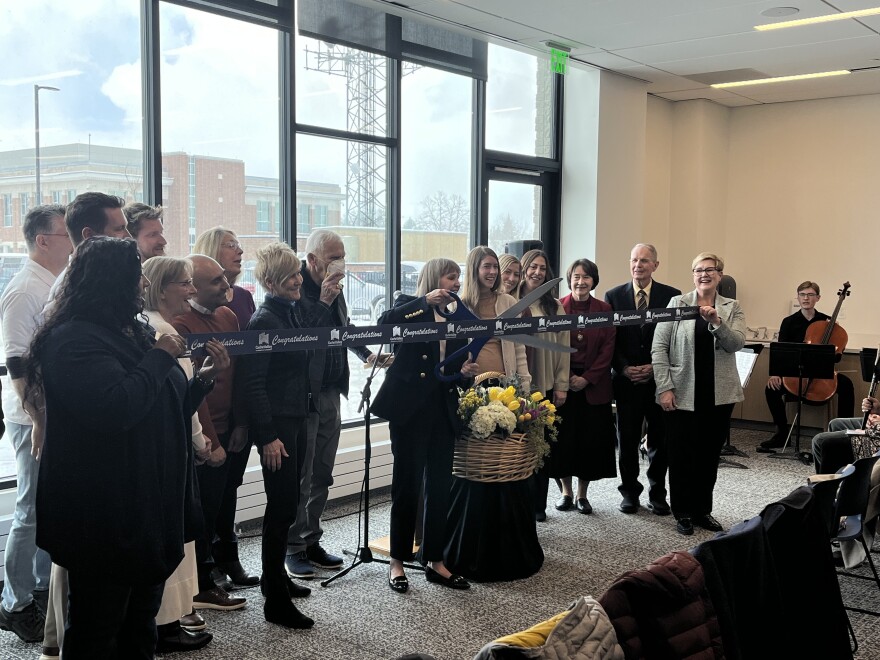 A group of people are surrounding Logan Mayor Holly Daines, who is holding a large pair of scissors, before she cuts a ceremonial ribbon in the new Logan Library. 