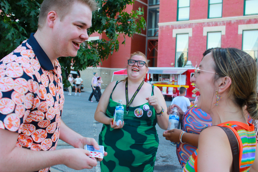 Magician Christian Manahl performs a close-up magic card trick for a group of people at a Pride event in Naftzger Park.