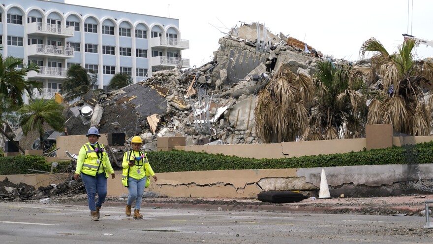 Workers walk past the collapsed and demolished Champlain Towers South condominium building in Surfside, Fla., on Tuesday.