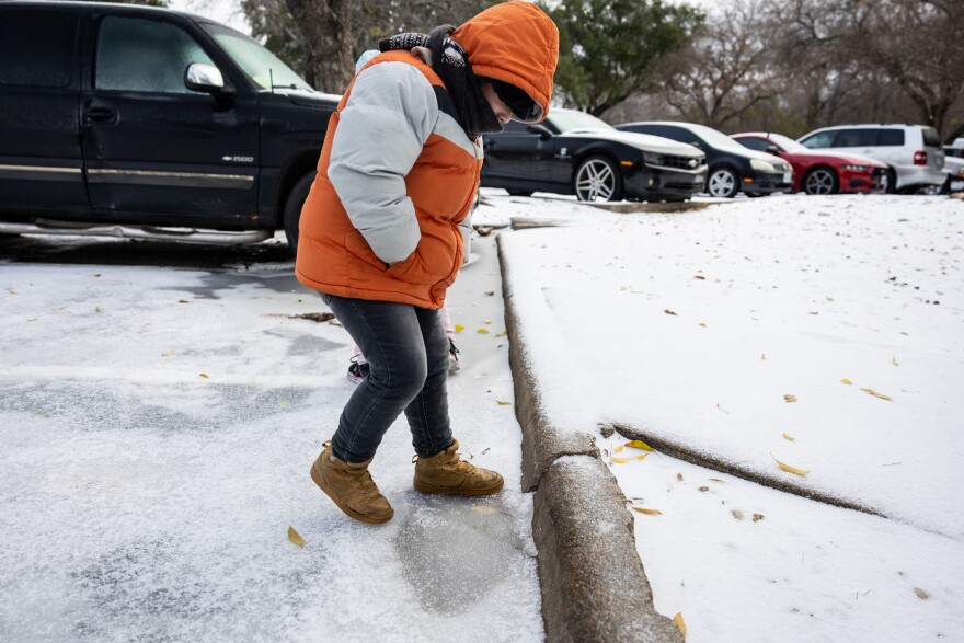 A boy dressed in a coat and hat stand on ice in a parking lot.
