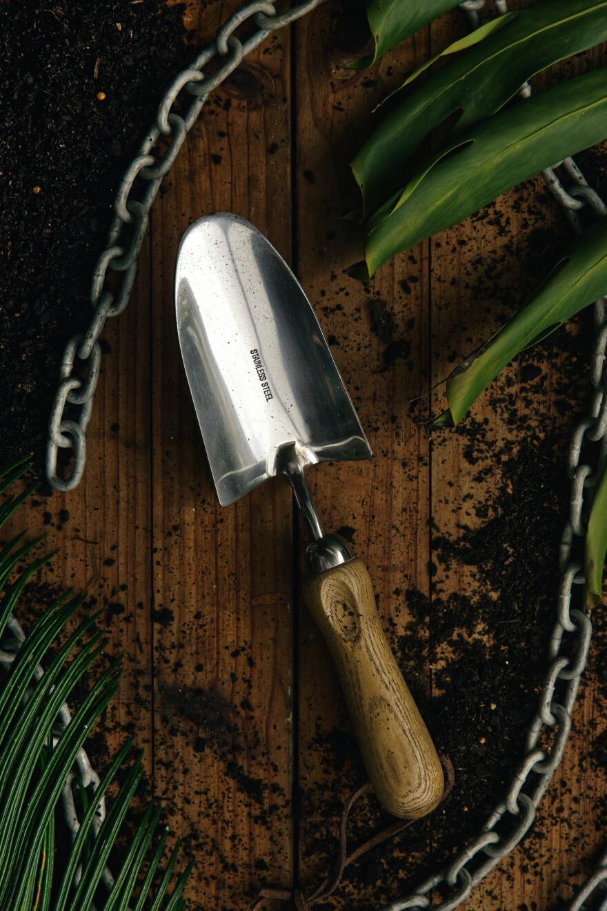 A garden spade on a dirt-strewn wood tabletop with a chain and green plants around the edges of the frame 