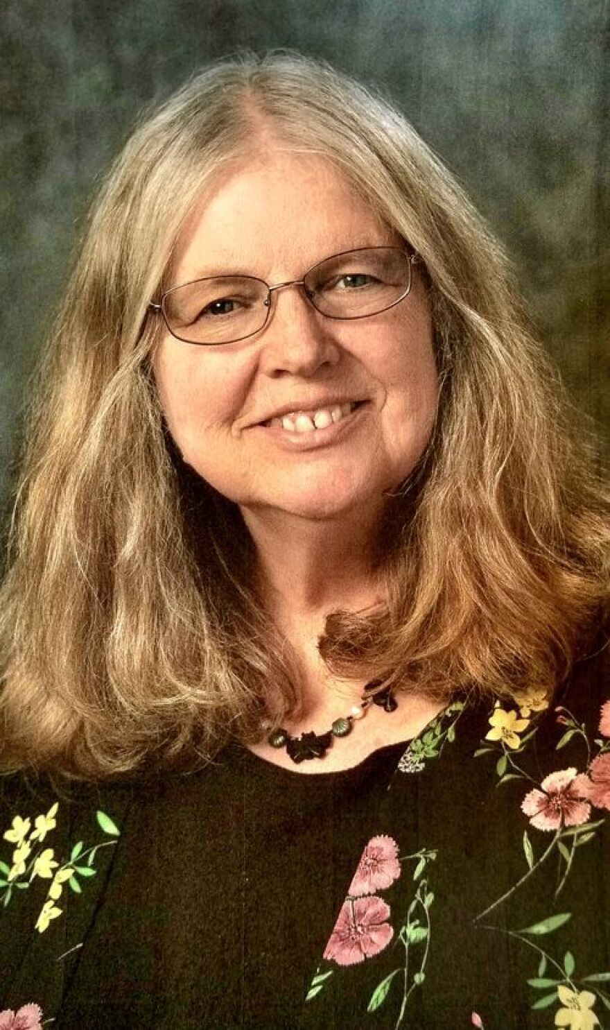 A woman with shoulder-length sandy colored hair and glasses smiles for the camera.