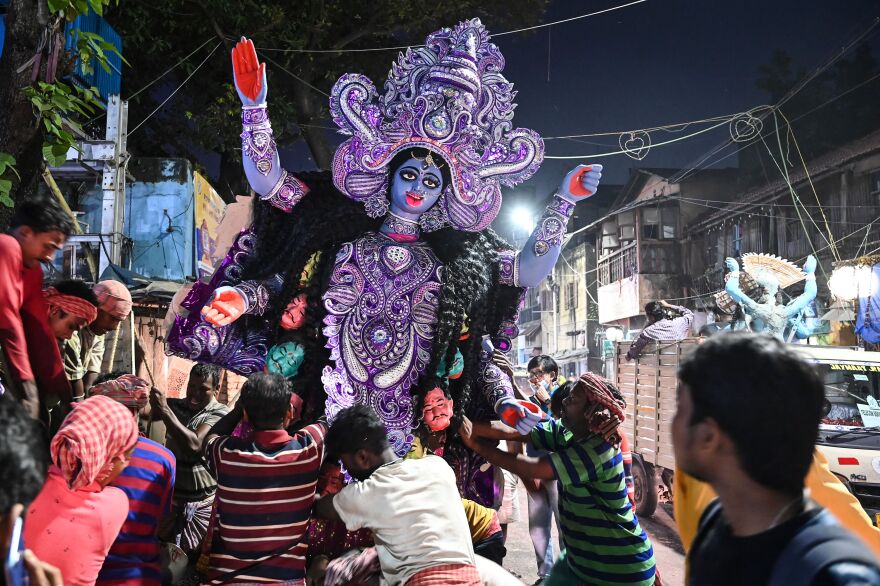 People carry a large purple statue of a Hindu goddess down the street against a dark sky.