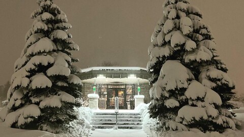 The KAXE studio against a dark sky flanked by snow covered balsam trees. 