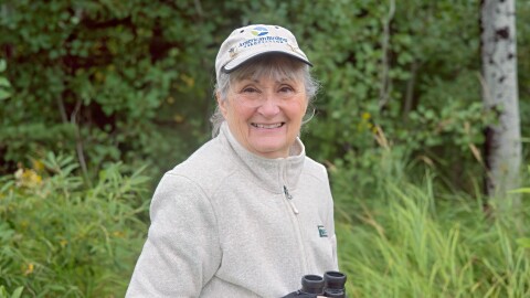 Woman holding binoculars in a green, natural area