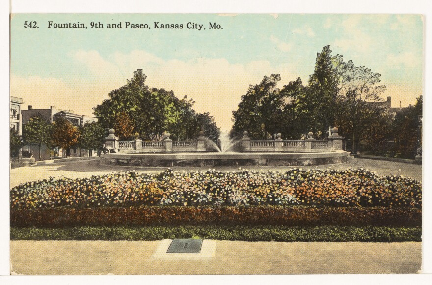 Postcard with a watercolor drawing of an oval fountain with a center spray, with white and yellow flowers in the foreground.