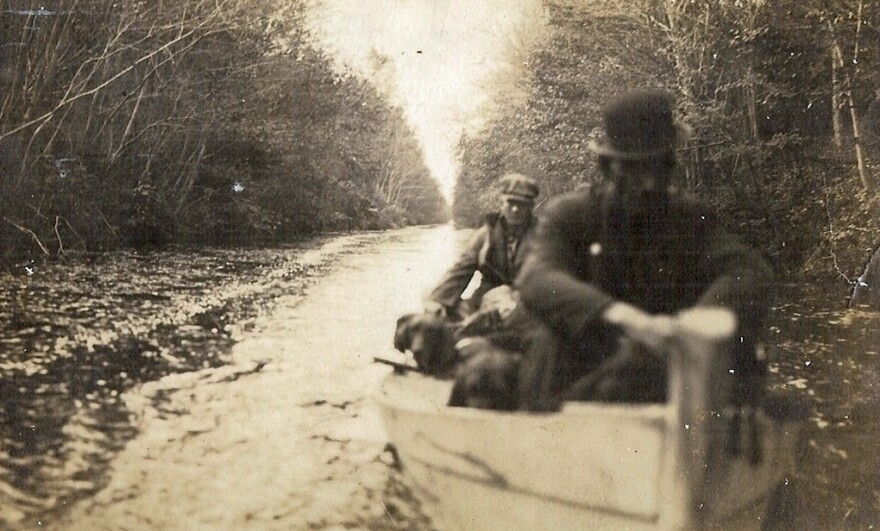 Chief Jesse Bass at the bow of a john boat loaded with hunting dogs. He often guided groups of hunters for longer trips on a barge up canals in the Great Dismal Swamp. (circa 1930s)