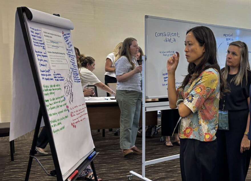 A woman in a floral shirt looks at a big notepad with writing in different colors. Others do the same behind her.