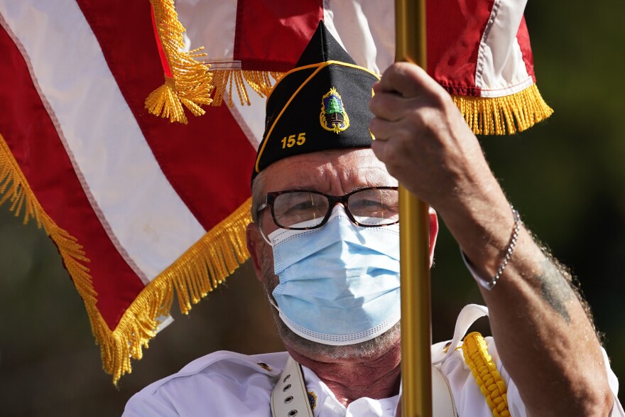 Brent Brown, sergeant-at-arms of the American Legion Post 155, wears a face covering to help prevent the spread of the coronavirus while holding the American flag during a Veterans Day ceremony, Wednesday, Nov. 11, 2020, in Naples, Maine.