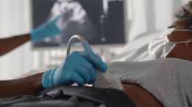 Close up of afro doctor examining patient pregnant woman with scanner. Afro-american pregnant woman in protective mask undergoing ultrasound test at gynecologist office