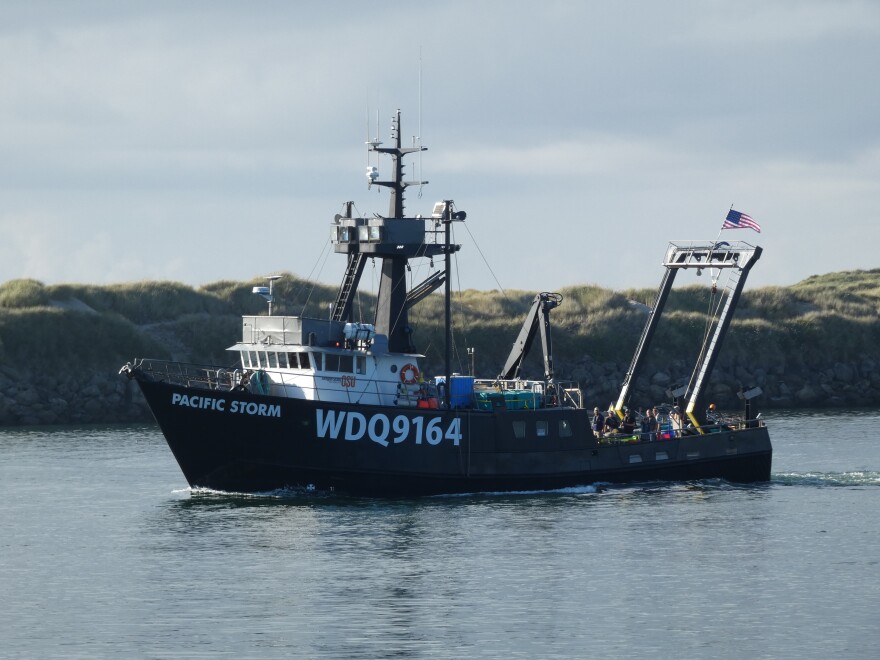 A research boat makes its way through calm waters past sand dunes.