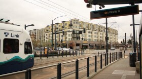 A massive multi-family apartment building with commercial retail spaces underneath. A train enters the photo in the foreground at the left of the frame.