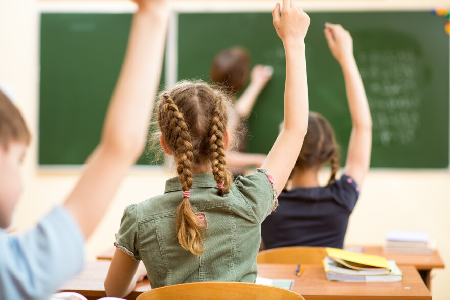 Students raise their hands in their classroom in this stock image.