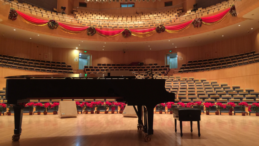  A concert hall with poinsettias lining the stage, with red bunting on the balconies and an amber glow. 