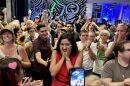 A woman places her hands on her face as people around her cheer