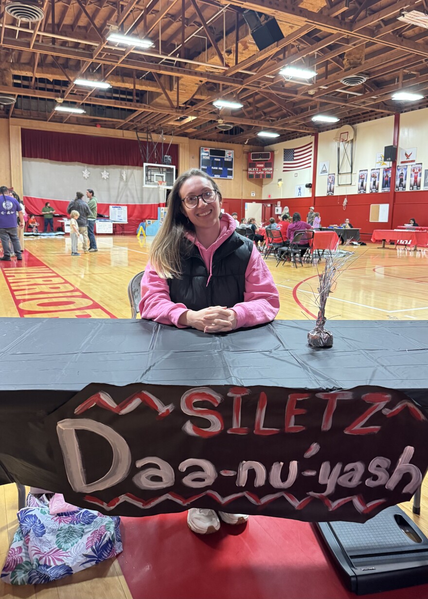Person sits a table with a sign that says "Siletz Daa-nu'-yash"
