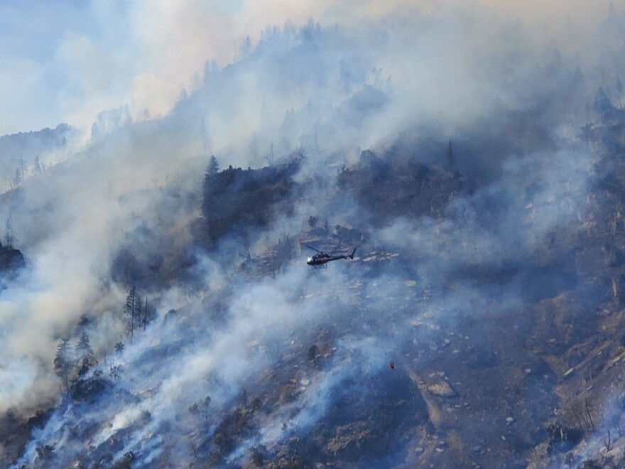 A helicopter flies over the smoke-filled, burn area in Glenwood Canyon during the Lake Christine Fire with a red bag hanging below the aircraft.