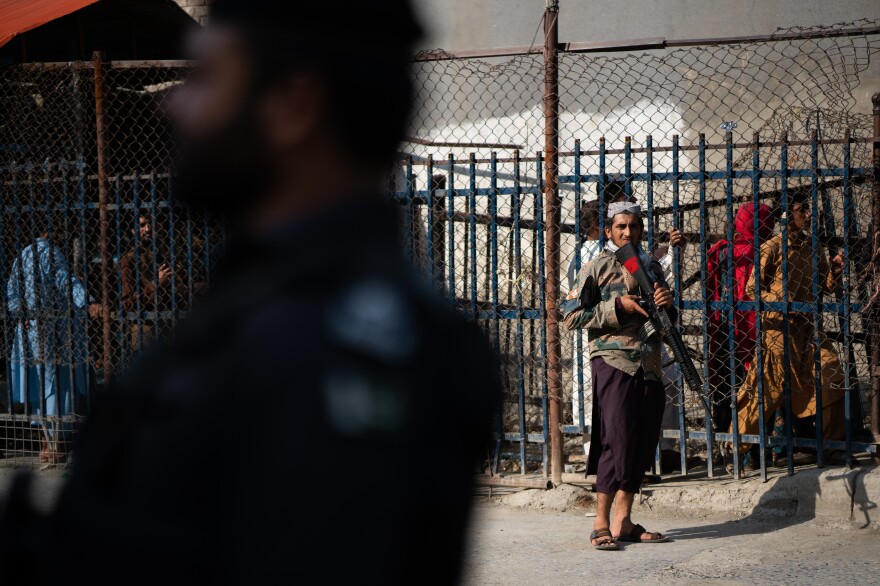 A Taliban guard stands on the Afghan side of the Torkham border crossing with Pakistan. People behind wait either to leave Afghanistan or to receive those returning to the country.