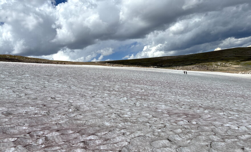 Two researchers stand on a vast ice patch in Wyoming’s Beartooth Mountains beneath large, dark clouds.