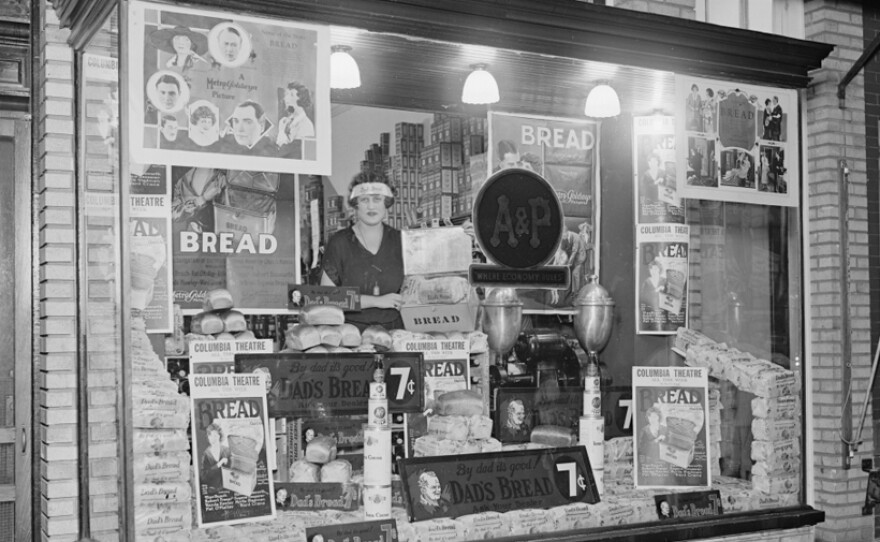 A woman stands in the bakery window of an A&P storefront, 1924.