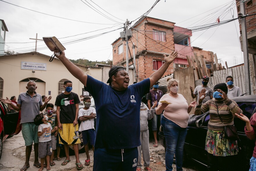 Pastor Deris of the evangelical charity Novos Sonhos prays before distributing meals in Peri Alto, a favela in São Paulo, Brasil. During quarantine lockdown, food donations helped folks survive. The count of COVID-19 cases in this favela has been low; masks are rarely seen. To encourage this preventive measure, the charity requires food recipients to mask up. <em>June 10. São Paulo.</em>