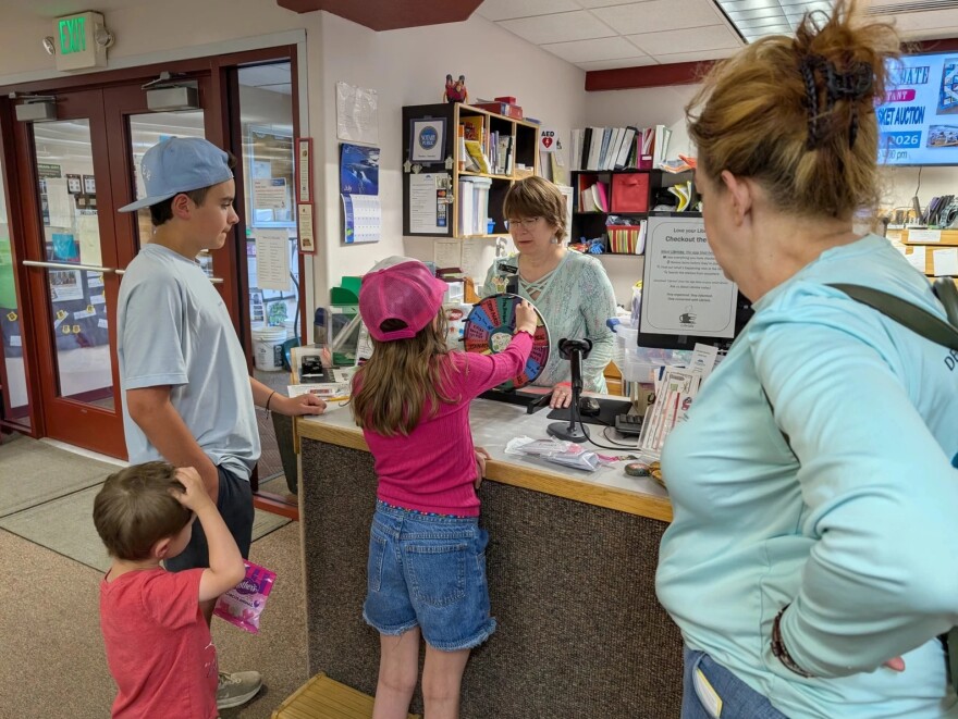 Delta Community Library Director Tiki Levinson, behind the counter, helps another family get rewards for reading.