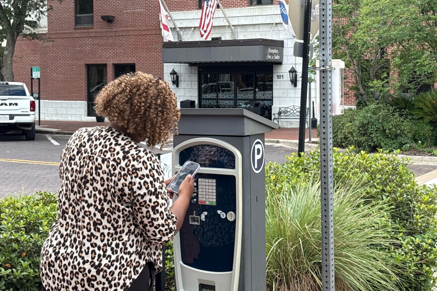 A woman uses her phone beside a downtown Gainesville parking pay station. The city began enforcing revised parking rates in September 2024 to make high-demand spaces available to more drivers.