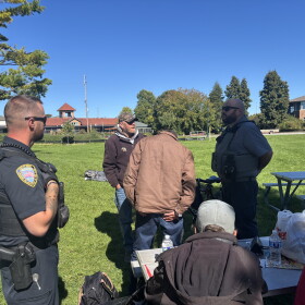 Traverse City Police Officer Matthew Kirkey and Police Support Services Worker Brad Neuder explaining the department's new enforcement efforts to a table of homeless individuals at Hull Park (Credit: IPR News / Maxwell Howard)